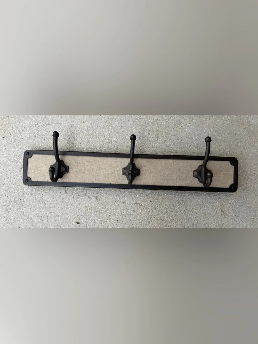 Hook rack features a dark bronze frame with a light-colored linen backing